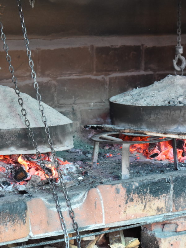 Traditional Bosnian cooking method 'Ispod Sača' with meat and vegetables being prepared under a metal lid covered with hot coals