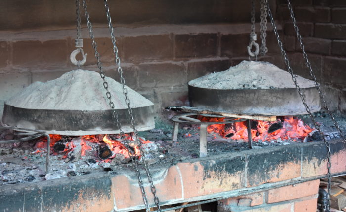 Traditional Bosnian cooking method 'Ispod Sača' with meat and vegetables being prepared under a metal lid covered with hot coals