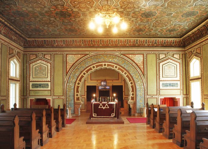 Interior view of the Ashkenazi Synagogue in Sarajevo, showcasing its richly decorated walls and ceiling, wooden pews, and the ornate ark.
