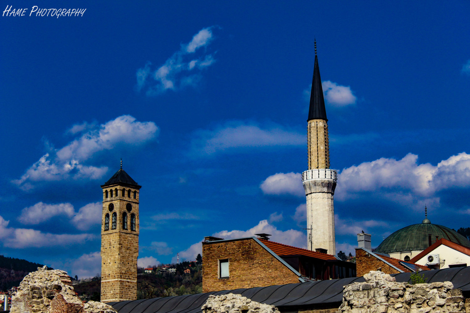 Minaret and bell tower against a blue sky in Sarajevo