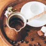 A copper džezva filled with freshly brewed Bosnian coffee on a tray with coffee beans, a white ceramic cup, and sweet treats.