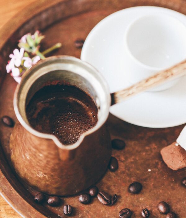 A copper džezva filled with freshly brewed Bosnian coffee on a tray with coffee beans, a white ceramic cup, and sweet treats.